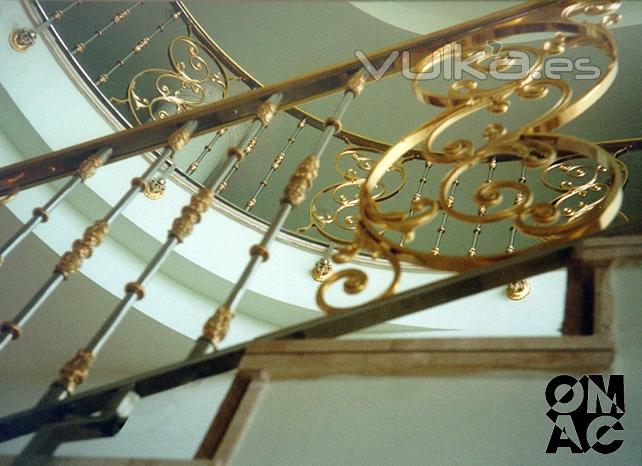 Barandilla de escalera con motivos ornamentales bañados en oro y balustres de inox.