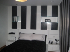 Dormitorio estucado en blanco, con el frente a rayas negras, terminado con decoracion textil a juego