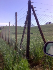 Cercado formado por malla st complementada con alambre de espino instalada en postes de madera