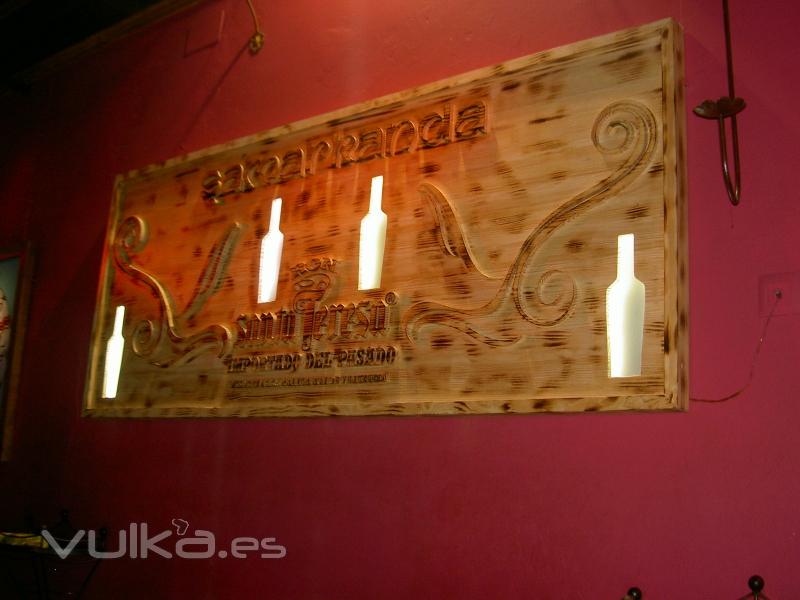 Tablero de madera fresado en bajo relieve con huecos para botellas iluminado.