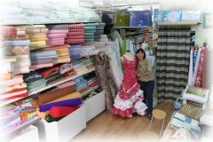 Conchi en su tienda, rodeada de sus telas, y con uno de los trajes de flamenca