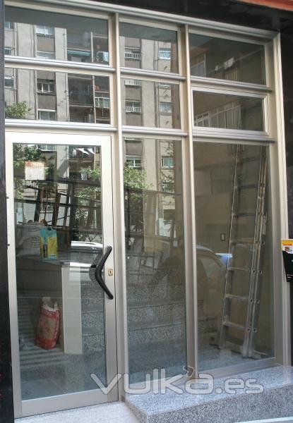 Puerta de comunidad en aluminio inox con travesaos reforzados y vidrio de seguridad laminar.