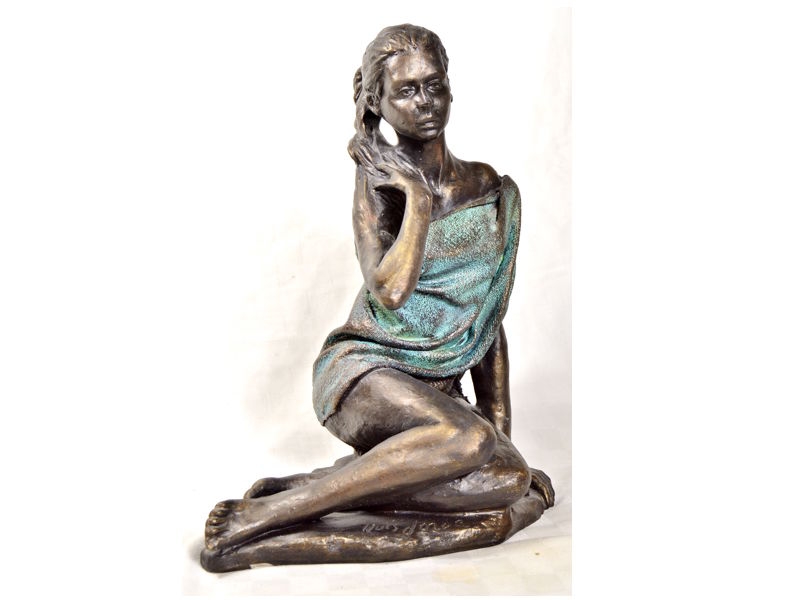 Figura o escultura de bronce, de joven sentada cubierta con toalla o pareo. Llus Jord.