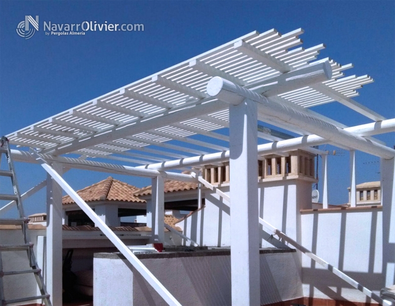 Montaje de pérgola en palo redondo tratado en autoclave con cubierta alistonada en blanco.