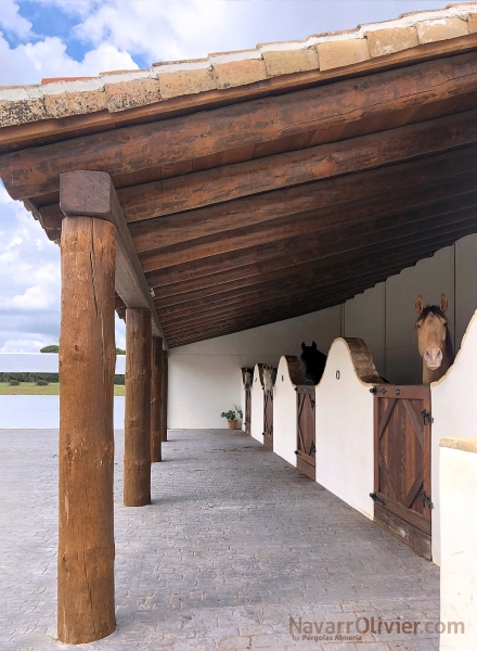 Pérgola de tronco y madera con cubierta de teja para cuadra de caballos 