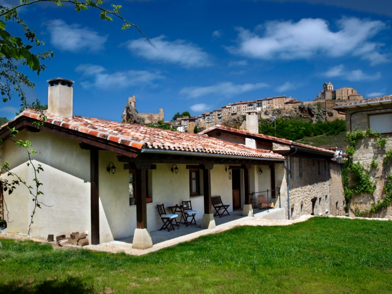 Vista exterior de la vivienda, con el jardín, el porche y el perfil de Frías al fondo