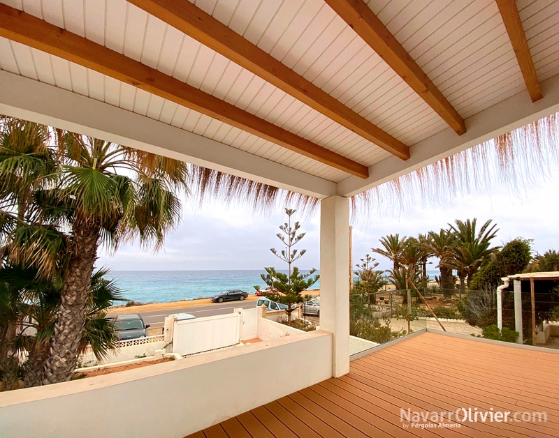 Terraza cubierta por pérgola de madera con friso blanco con remate en carritx natural