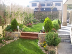 Diseño de jardín con césped antural y mezcla con jardineras de piedra y plantas.