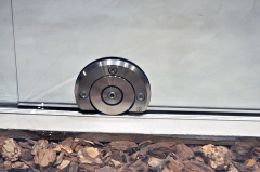 Rodillo ubicado en medio, bajo la hoja de la puerta y sujetado por dos semicascarones de acero inoxi